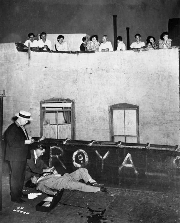 Forensic detectives take the fingerprints of murdered store owner Joseph Gallichio, as he lies on the roof beside his cage of racing pigeons. 12 East 106th Street, 1941