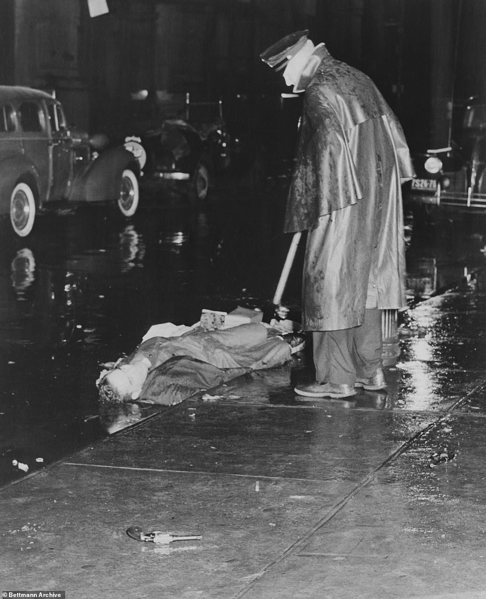 A policeman looks at the body of Louis Riggiona, found dead in the gutter of Mulberry Street with two bullets in his heart and the two murder weapons abandoned nearby