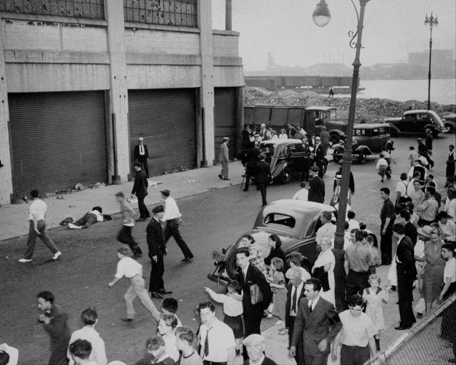 A crowd gathers around the body of John Masseria, Joe "The Boss" Masseria's brother, as police arrive at the murder scene on 19th Street. 1937.