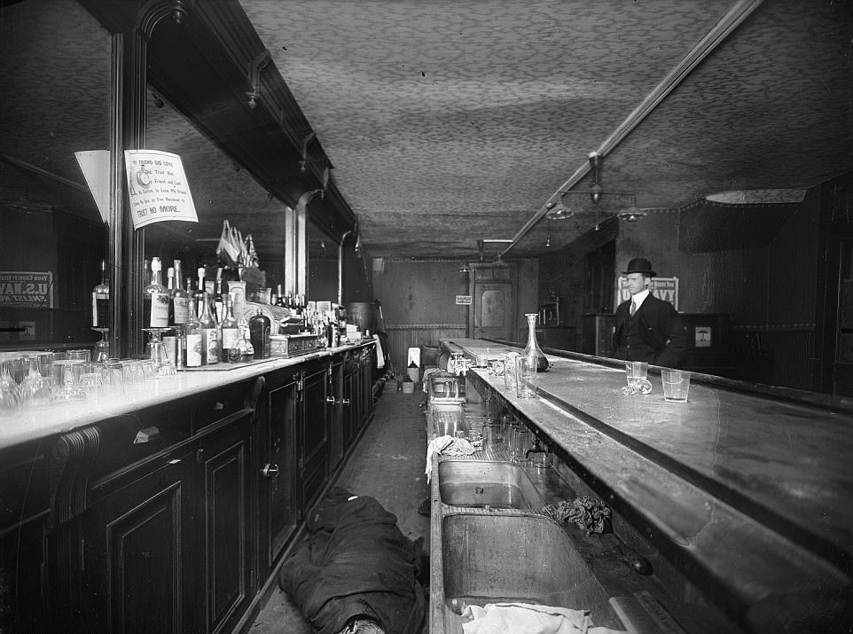A piece of paper over the body of a man in a bar says 'trust no more', early 1900s New York