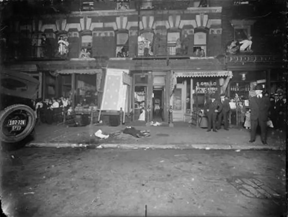 Onlookers lean out of tenement windows to view a man's body on the sidewalk, 1916-1920