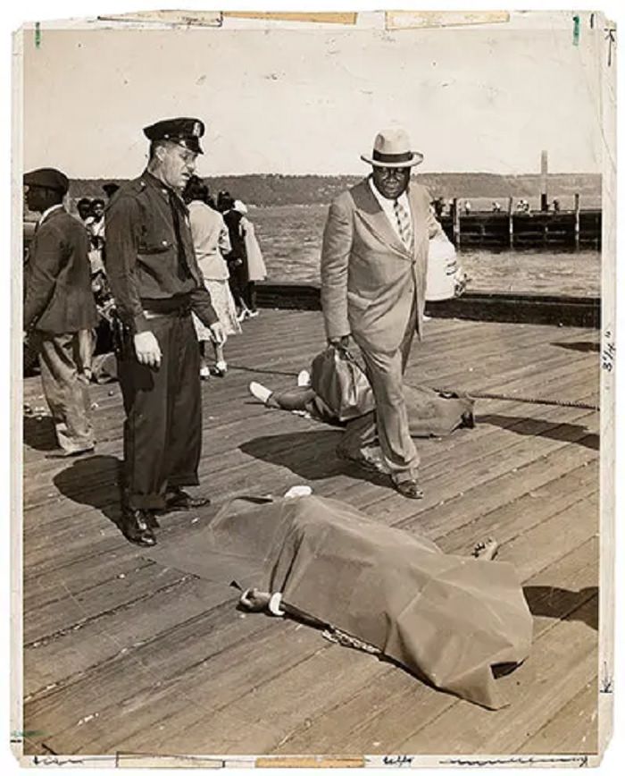 Police officer and lodge member looking at blanket-covered body of woman trampled to death in excursion-ship stampede, 18 August 1941