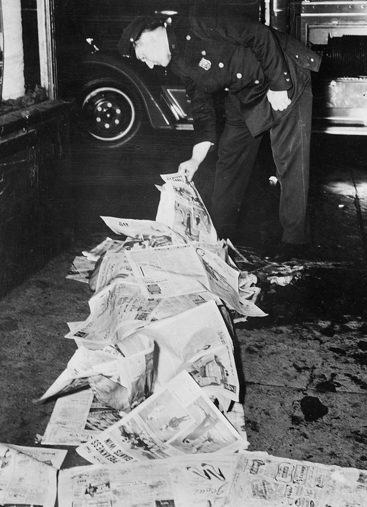 A policeman inspects the body of a murder victim covered with newspaper in New York City, 1943