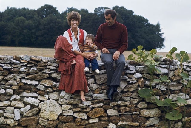Jane Fonda sitting on a stone wall.