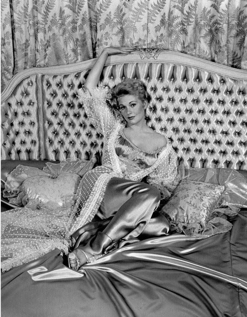 Kim Novak, lounging on satin bed.