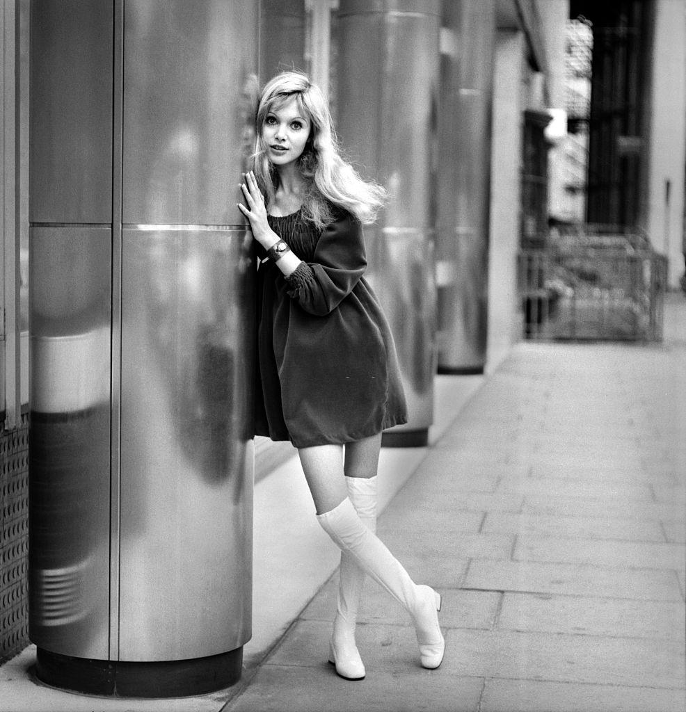 Madeline Smith in a black dress and fwhite knee high boots, 1969