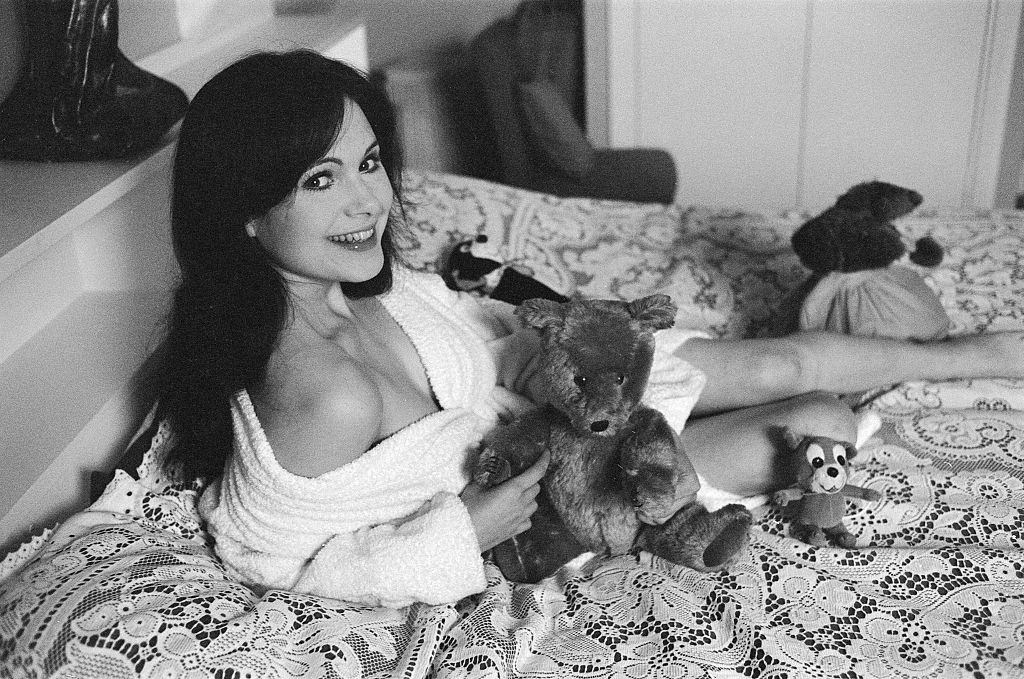 Actress Madeline Smith poses on the bed with her teddy bears, 1973