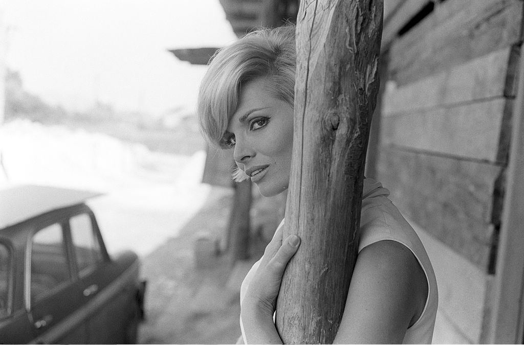 Scilla Gabel posing behind a wood pillar covering her neck, Italy, 1965.