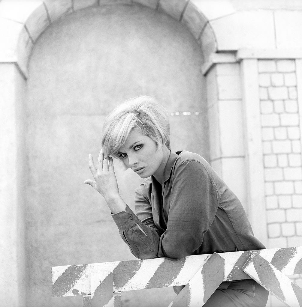 Scilla Gabel leant against a wood barrier, with her right hand in her hair, 1965.