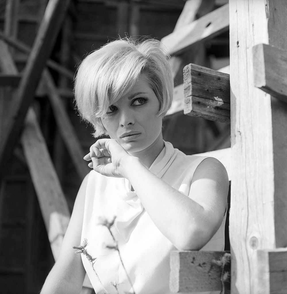 Scilla Gabel leaning on a wood beam and is wearing a light colored blouse, 1965