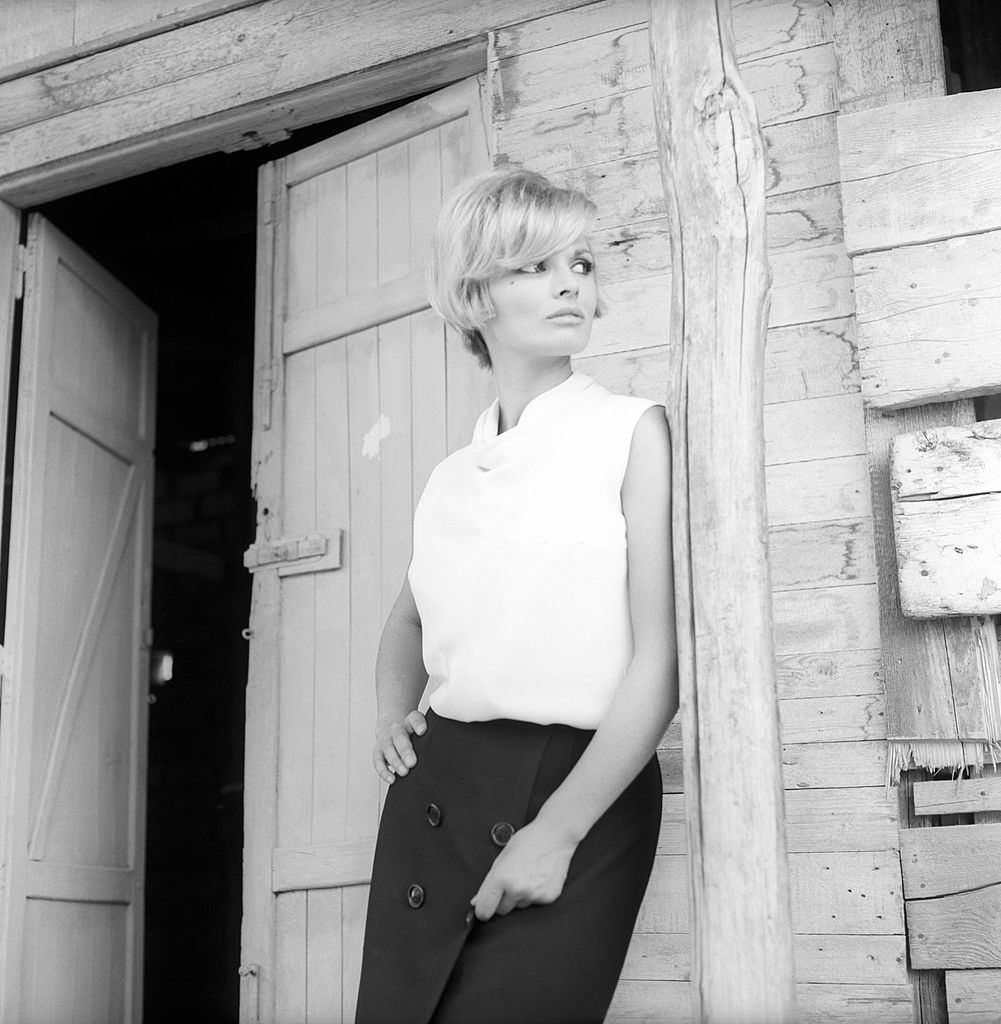 Scilla Gabel leant against a wood pillar in front of the open door of a barn, 1965