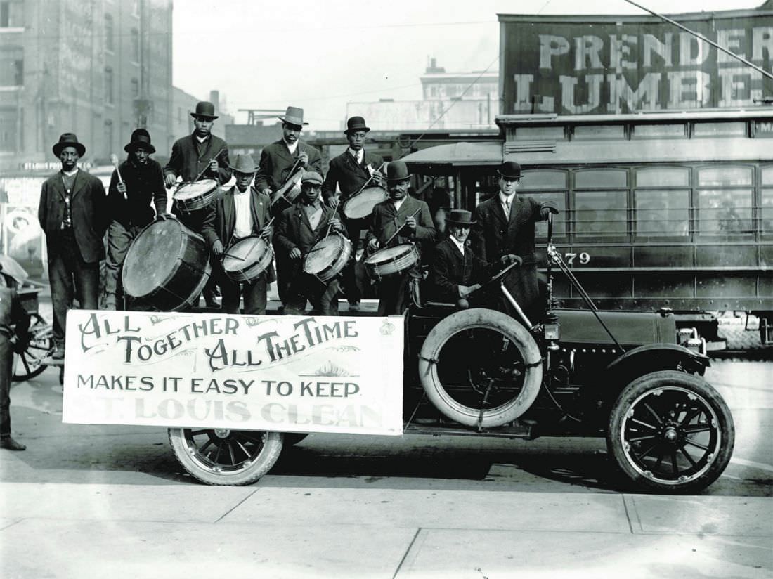 An African-American drumming group perform on the back of a truck carrying a banner that reads “All Together All the Time Makes It Easy to Keep St. Louis Clean” on Market Street, 1912