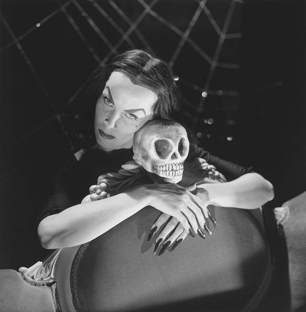 Maila Nurmi in character as Vampiria with her arms around the skull-topped back of a chair, 1950s