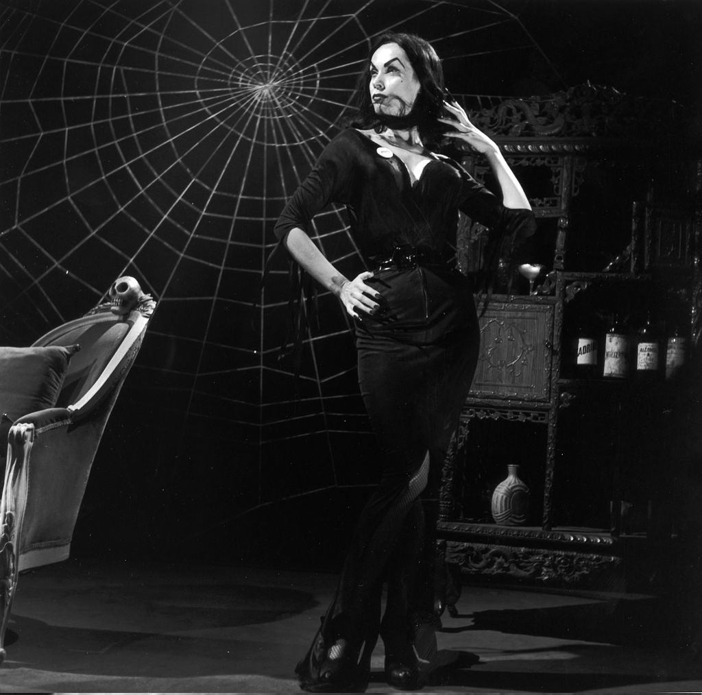 Maila Nurmi posing on a horror set with a wooden armoire, a skull-topped chair, and a spider web, 1956