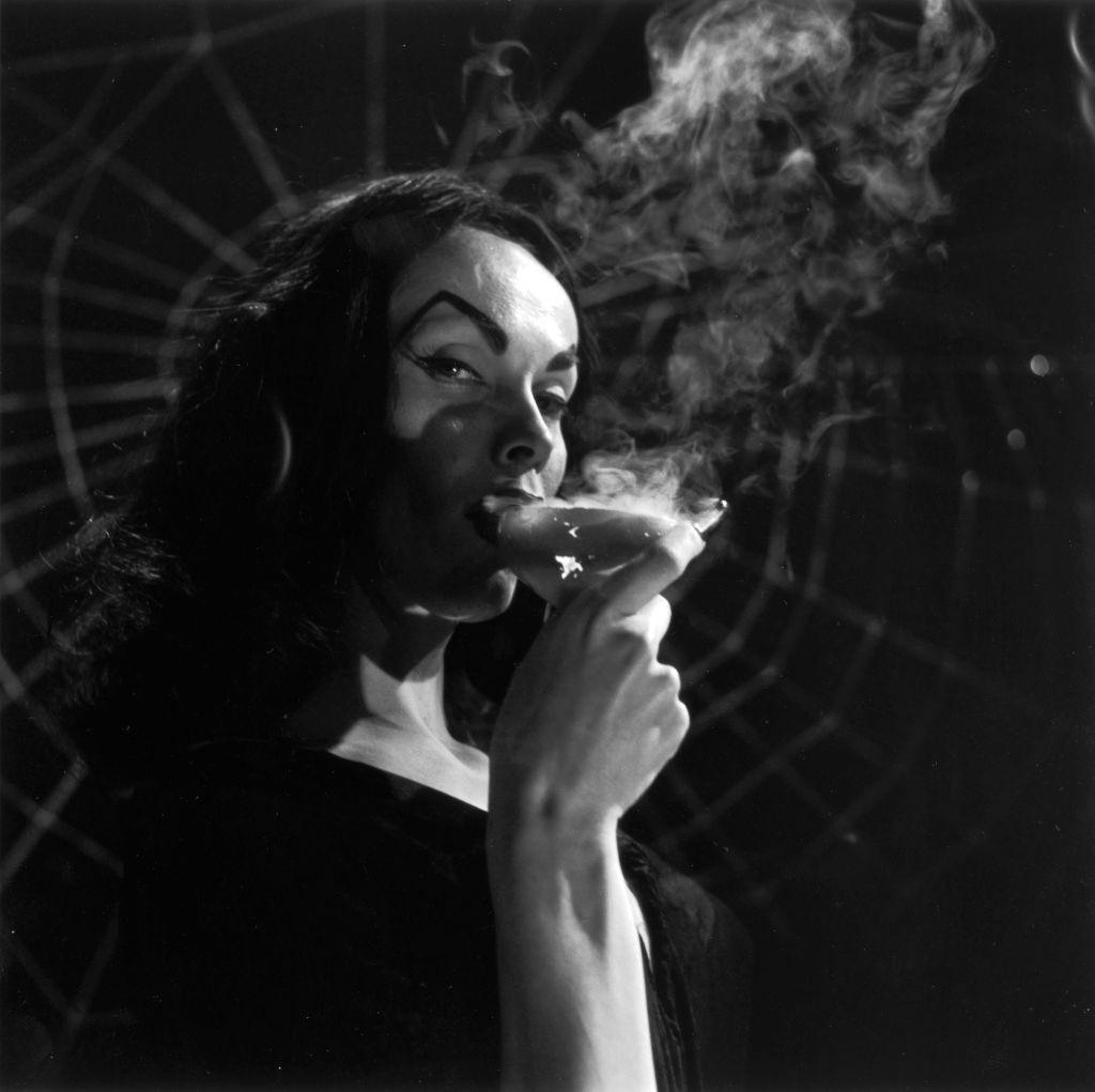 Maila Nurmi drinking from a smoking cocktail glass in front of a spider-web, 1956