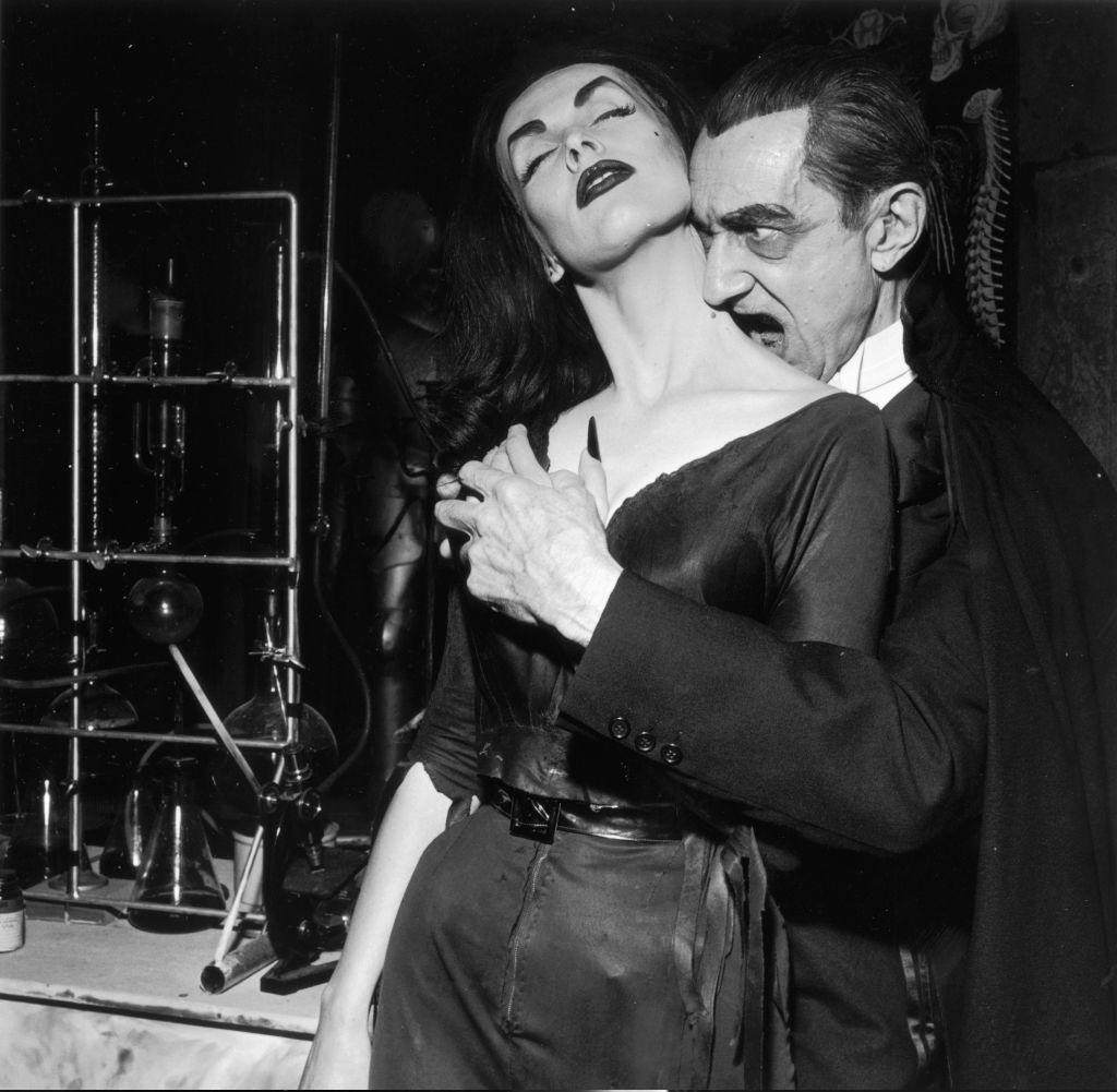 Bela Lugosi playing Dracula, prepares to bite into Finnish-born actor and television host Vampira's neck as they clasp hands, 1956