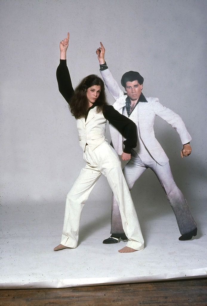 Gilda Radner posing with the portrait of John Travolta in a pose from the film 'Saturday Night Fever,' New York, late 1970s