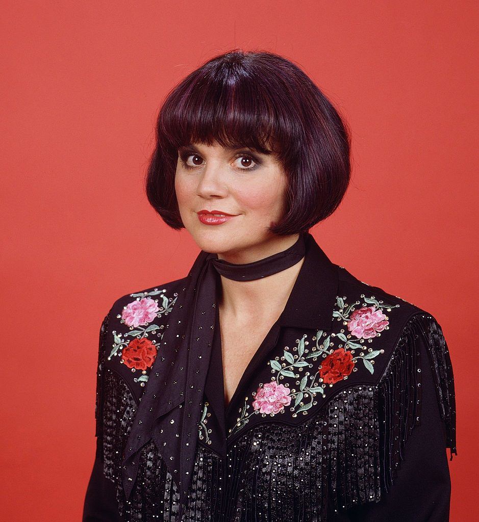 Linda Ronstadt wearing an embroidered, fringe shirt with a sequinned scarf around her neck, 1987