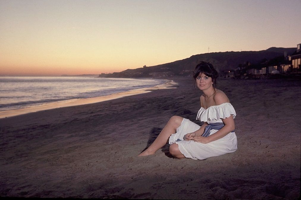 Linda Ronstadt sitting on beach.