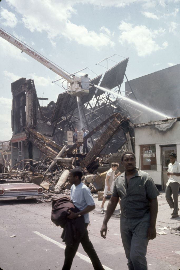 Kilátás egy tűzoltóknak, amikor egy lángokkal küzdenek, amikor a gyalogosok sétálnak alattük folyamatos zavargások nyomán, Detroit, Michigan, 1967