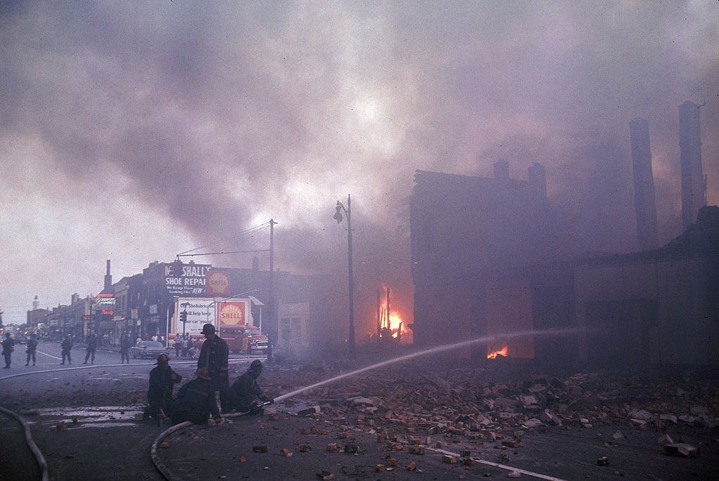 A tűzoltókat rendőrség védi, míg a dohányzó lángokkal küzdenek, miután a verseny zavargása megrázta a várost, 1967