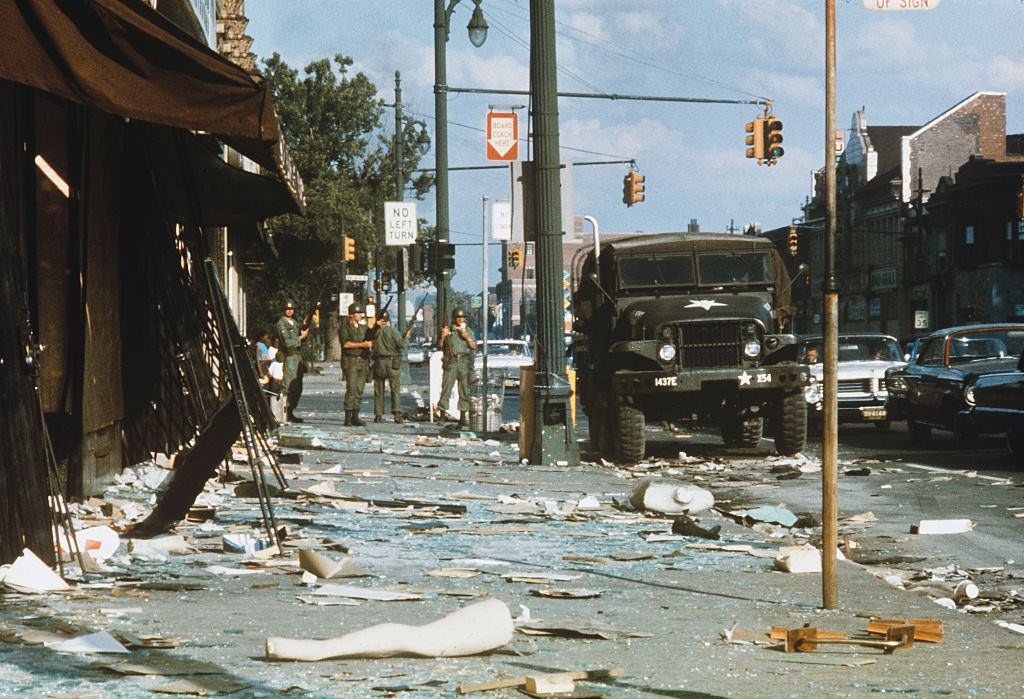 National Guardsmen armed with rifles stand guard amid debris littering the streets of the West Side of Detroit, 1967