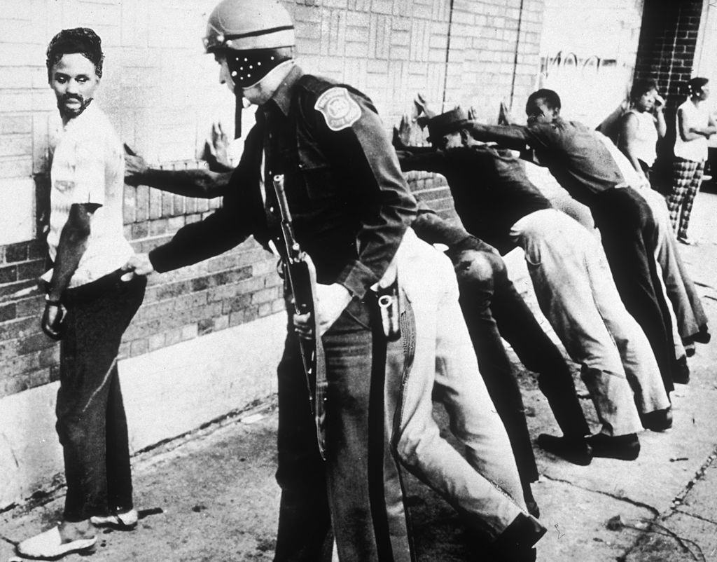A rendőrség egy afroamerikai férfit tör, miközben más gyanúsítottak a falnak támaszkodnak az 1967. évi 12. utcán