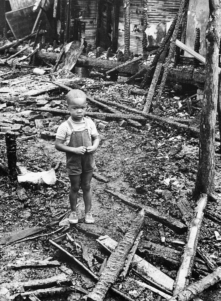 Three year old Thomas Allen stands the ruins of his home on Detroit's east side, 1967