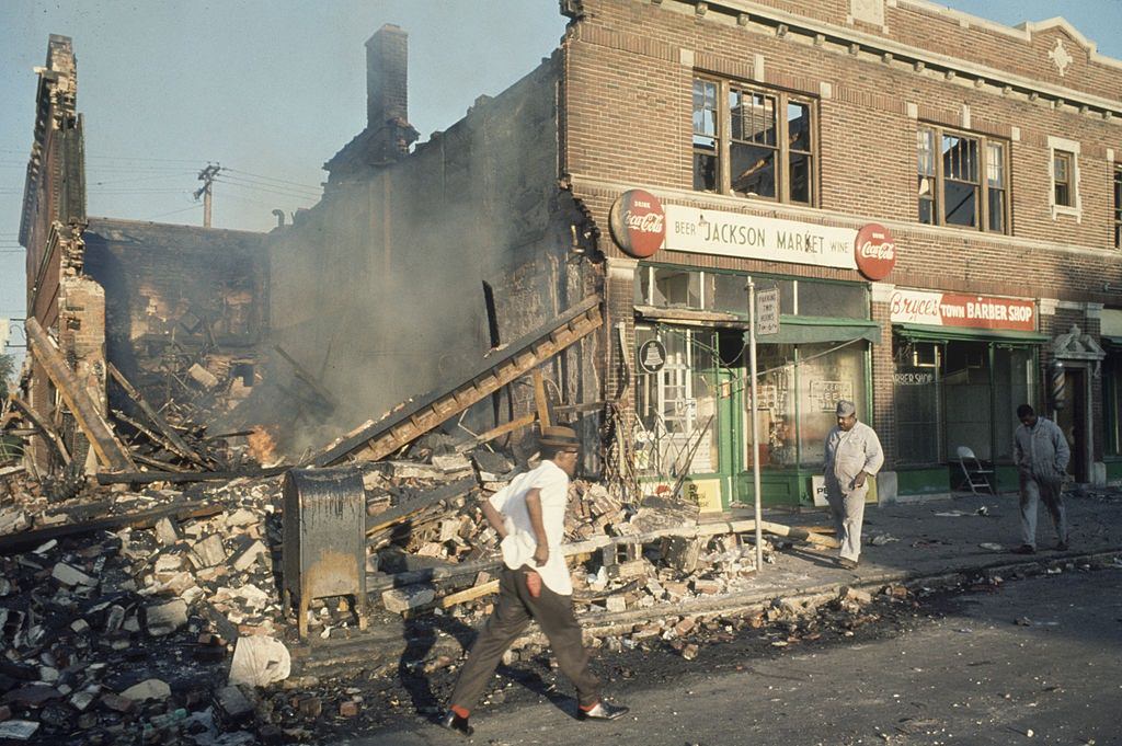 A Detroit police officer stands on an end-cap in a grocery store to guard against additional looting during riots in Detroit, 1967
