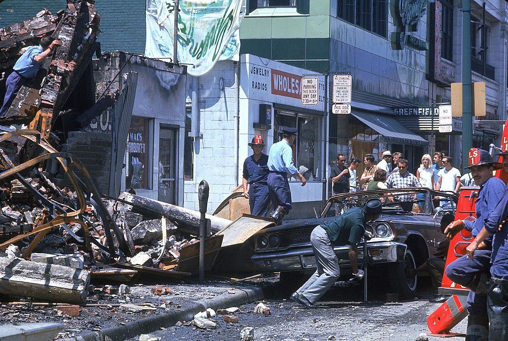 A group of onlookers gather to watch authorities clean up debris after fires during riots in Detroit, 1967