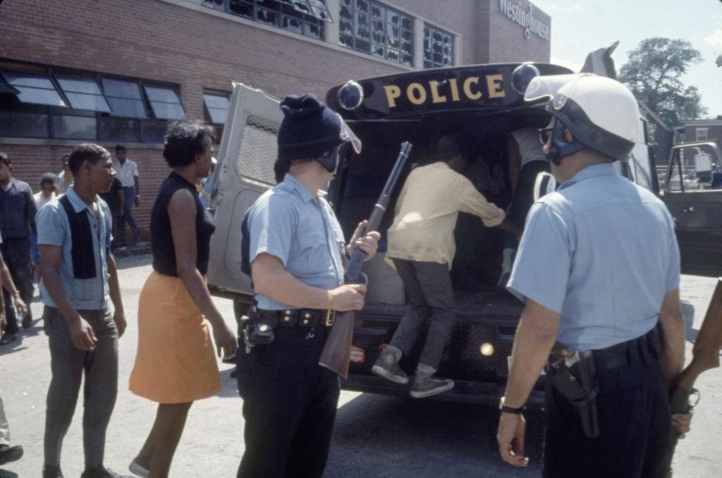Police officers load suspects into a police van in the wake of ongoing riots , Detroit, Michigan, 1967