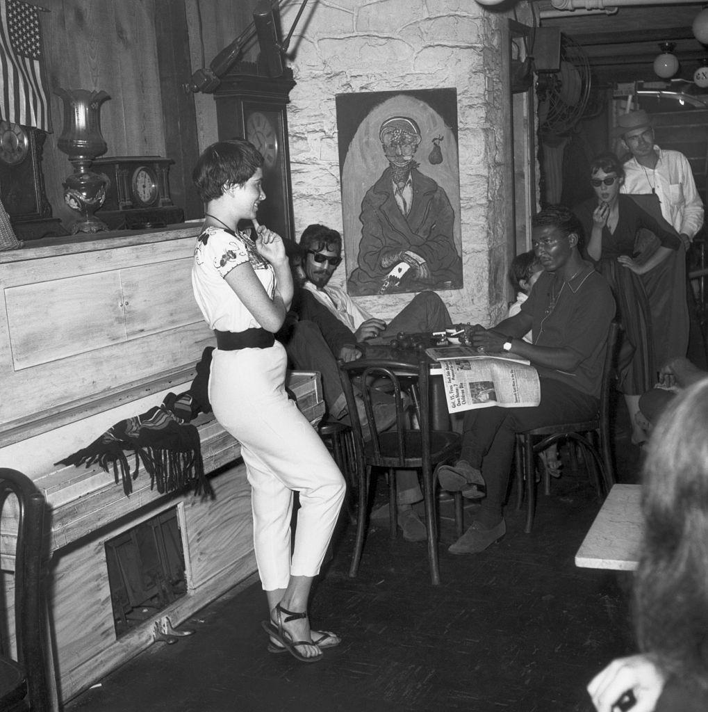 A beatnik woman stands in front of the entrance to the Gaslight Cafe, a center of beatnik poet life, in Greenwich Village, 1959