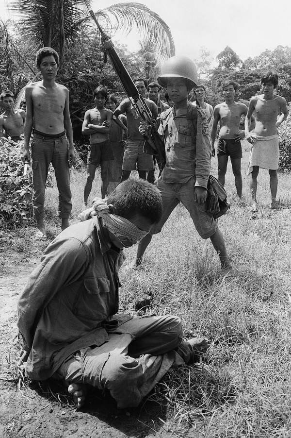 Gyerekkatona áll egy bekötött szemmel nézett katona felett, Angkor Chey, Kambodzsa.  1973-tól.