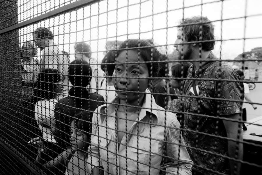 Refugees peer through the gate to the French Embassy, begging to get in, Phnom Penh. 1975.