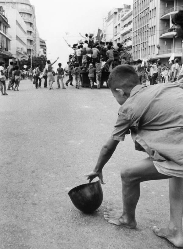 Egy fiatal fiú felveszi a katona sisakját, amikor a győztes Khmer Rouge a város utcáin, Phnom Penh, 1975-en esik át.