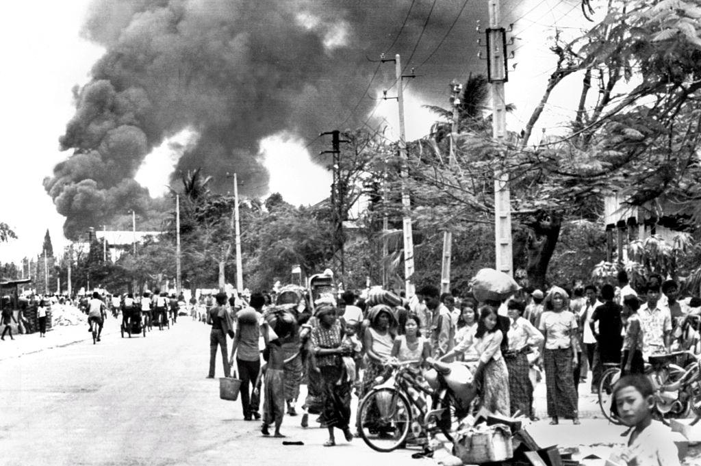 Cambodian inhabitants wait in a street of Phnom Penh, 17 April 1975 as the gasoline depot burns before the Khmer Rouge enter the capital and establish government of Democratic Kampuchea (DK).