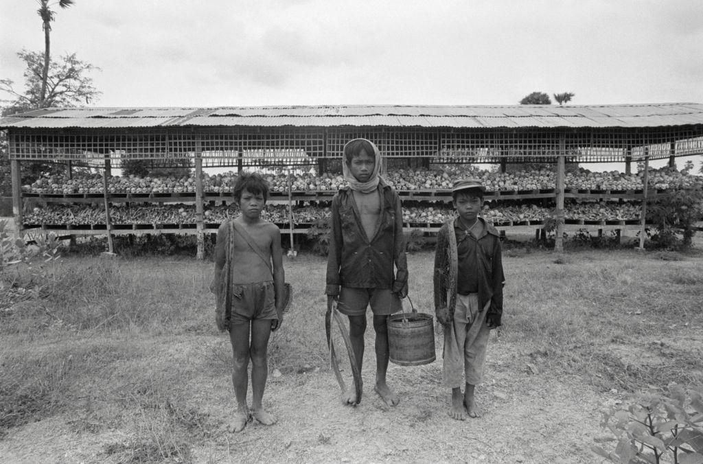 Mass Grave in Cambodia. The simple hut behind the three boys at the Choeung Ek extermination camp contains hundreds of human skulls and bones.