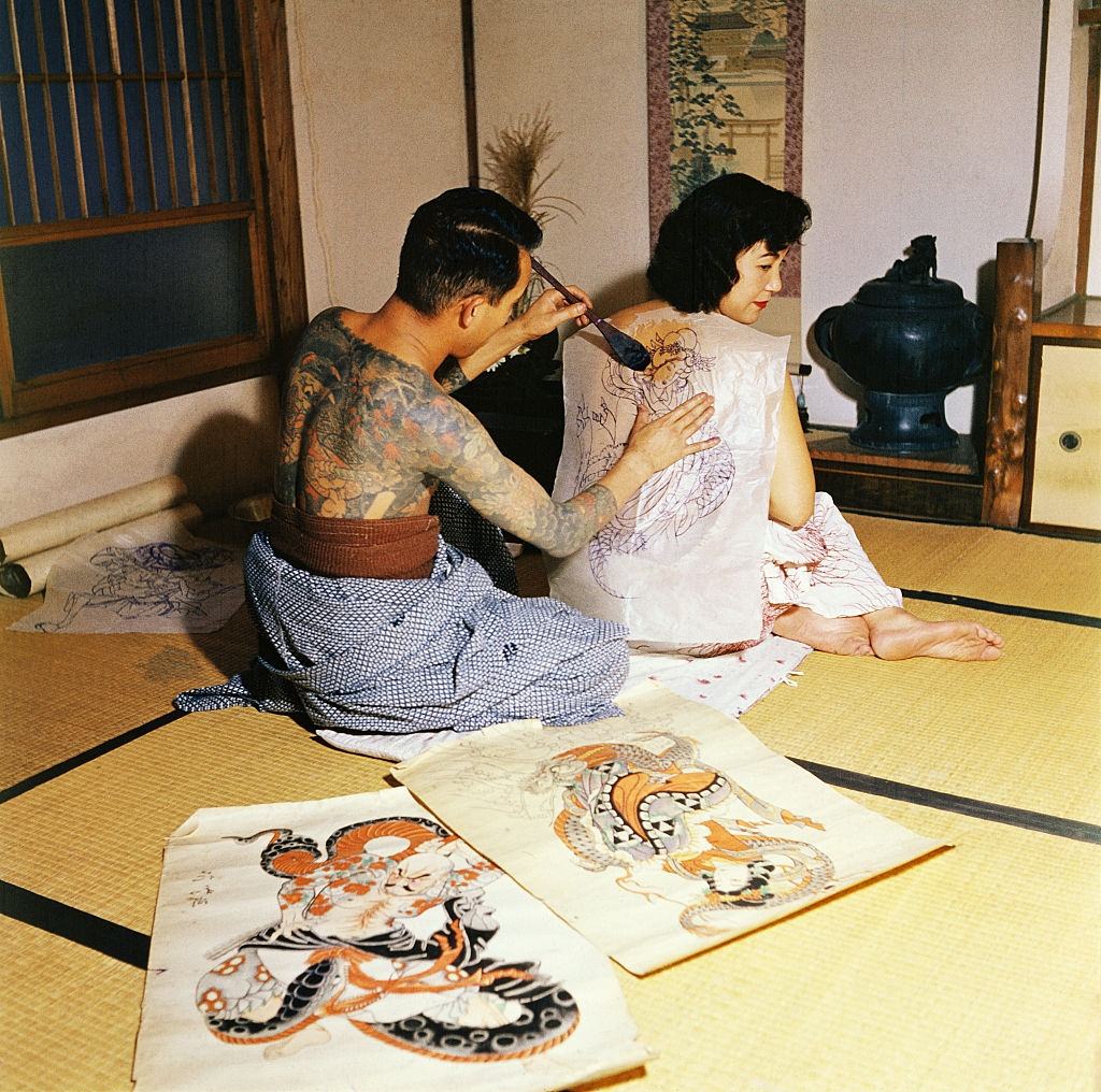 Japanese tattoo artist, Tokumitsu Uchida, with water brush, transferring picture chosen by customer as first step in tattooing design, 1955