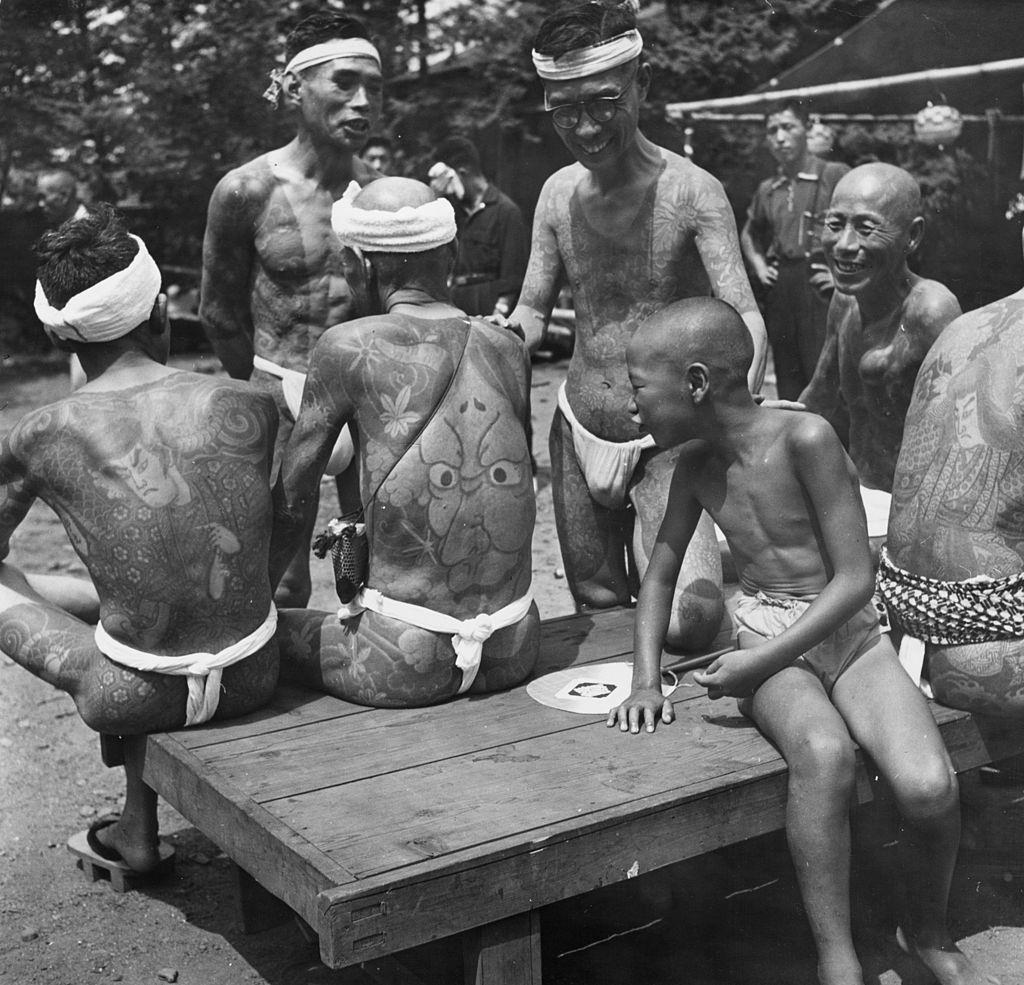 A young boy admires the tattoos on the backs of Japanese men at a rally held for tattooists and their clients to show off their 'designer' bodies, 1958