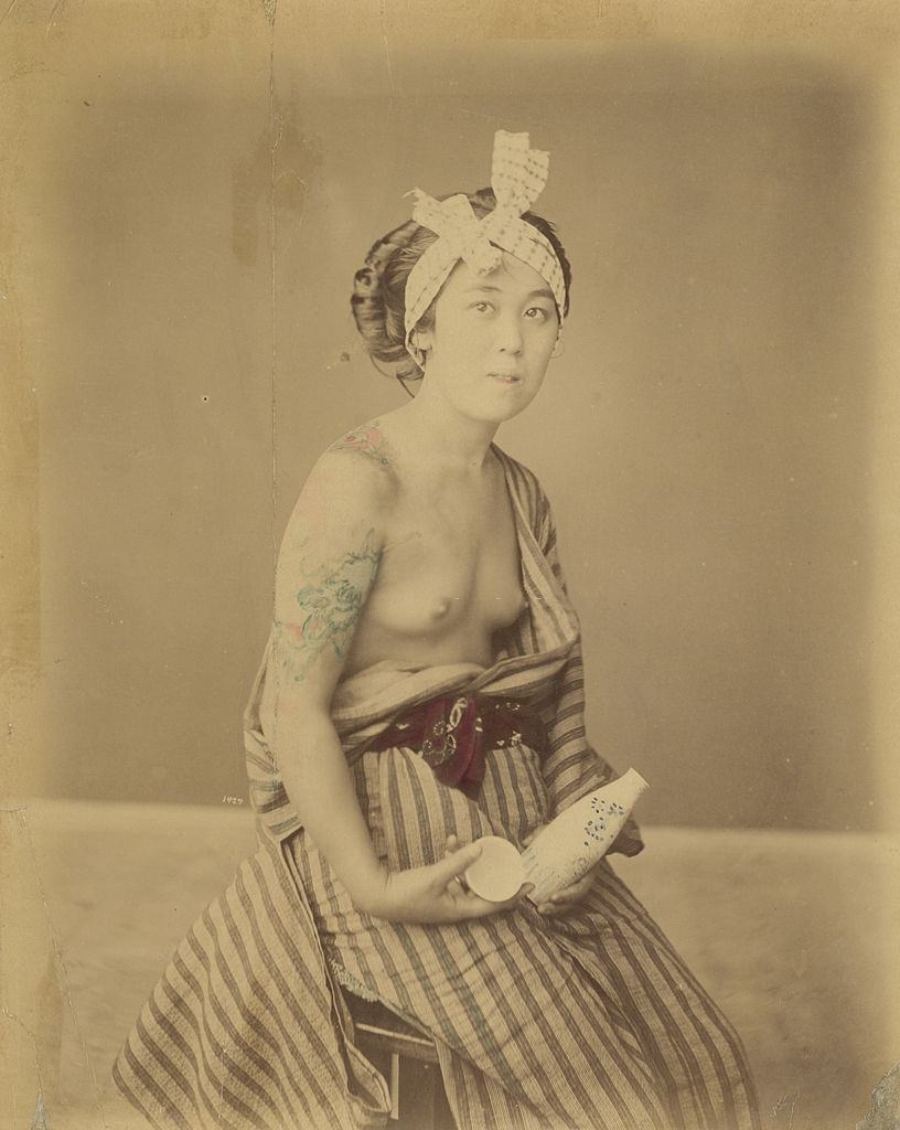 A young Japanese woman displays her tattoos, circa 1880