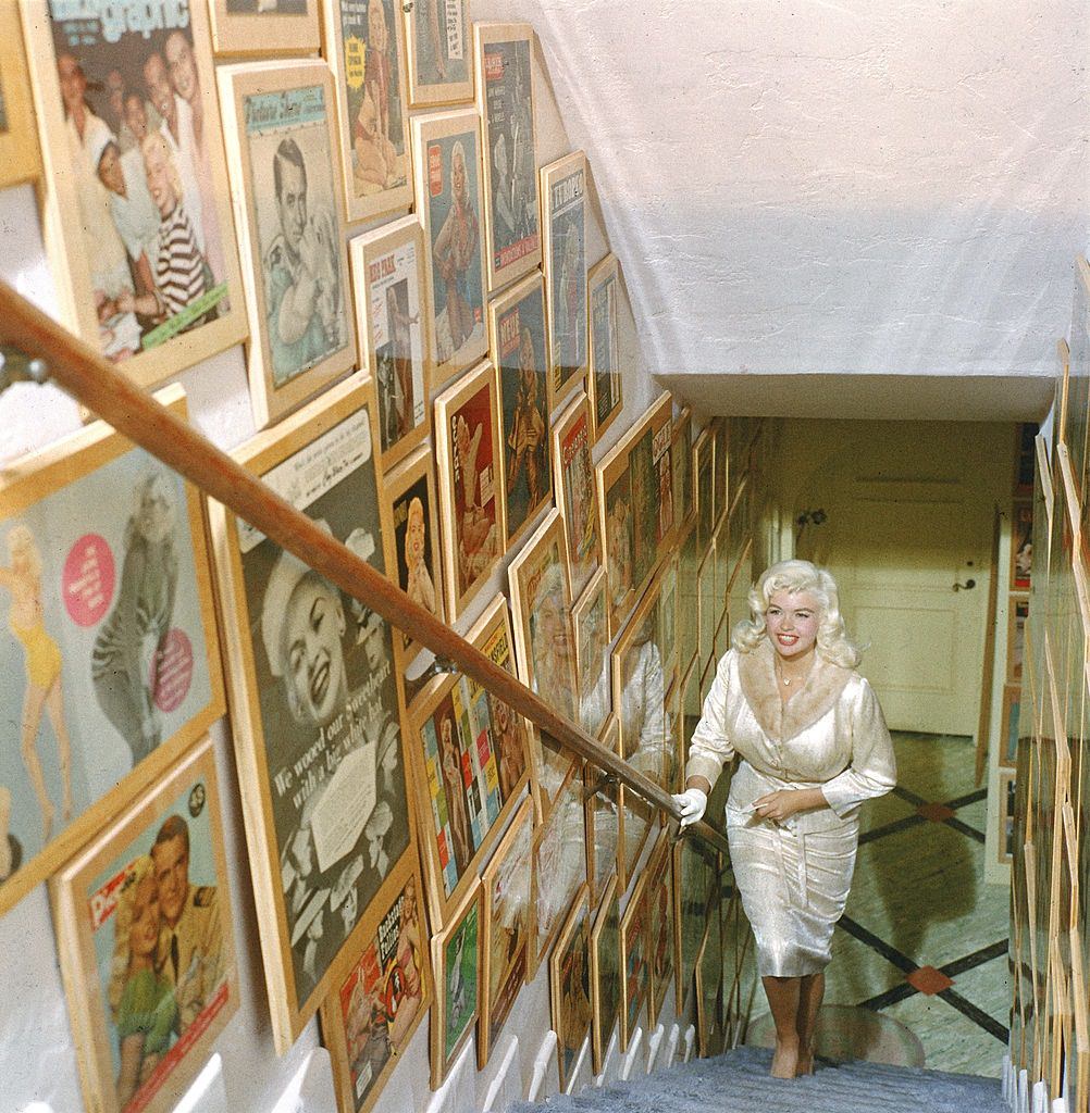 Jayne Mansfield walks up a poster-lined stairway in her lavishly decorated, Pink Palace, 1960s
