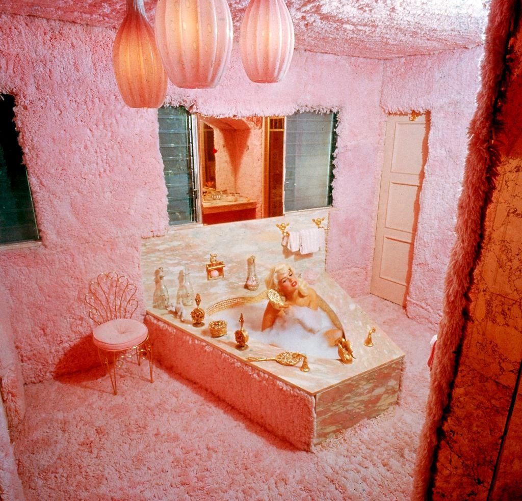 Jayne Mansfield combs her hair while sitting in a bubble bath in the pink carpeted bathroom of Pink Palace, 1960s