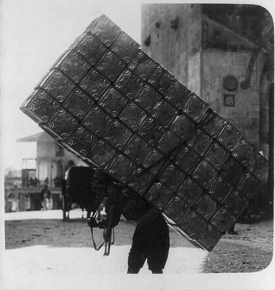 A porter carrying 50 empty petrol tins on his back, Circa 1914-1918