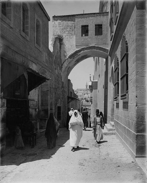 A woman walks below the arch of ecce, Circa 1898-1914.