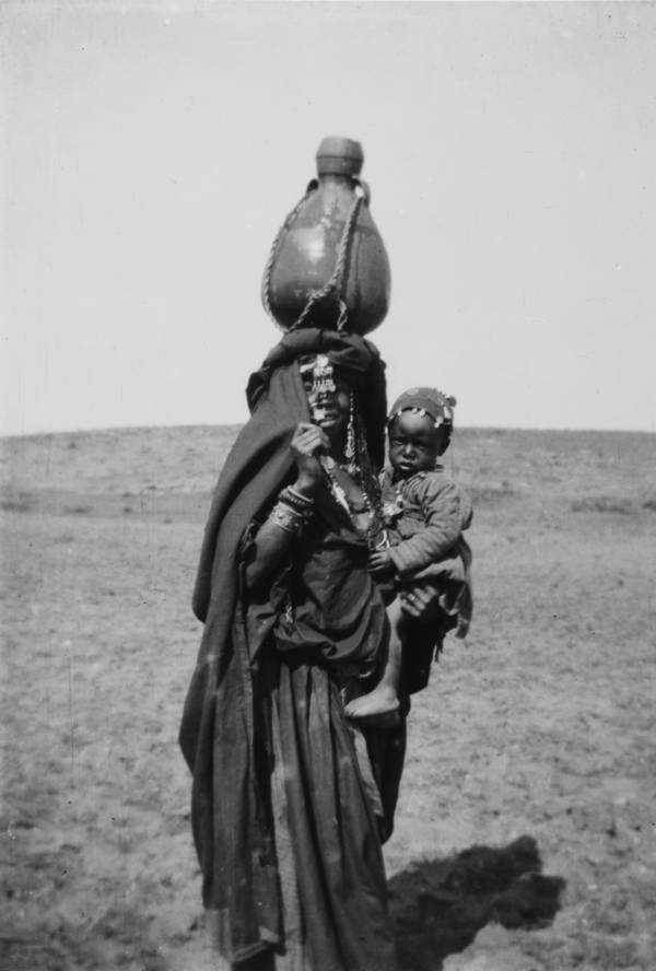 A mother carries her child with a jug on her head.Beersheba, Circa 1900-1920