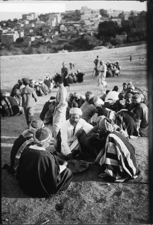 A group of people, labelled in the original caption as "natives," sit down for a meal, Circa 1900-1920