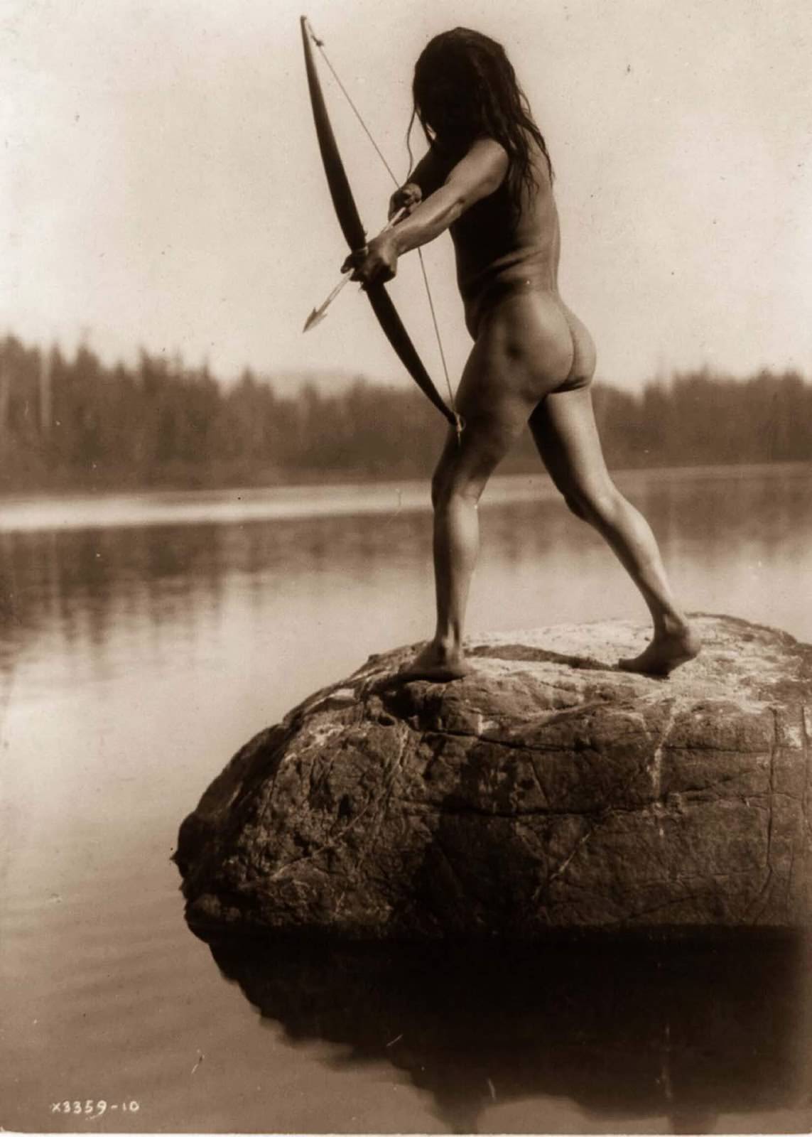 A Nootka man aims a bow and arrow. 1910.