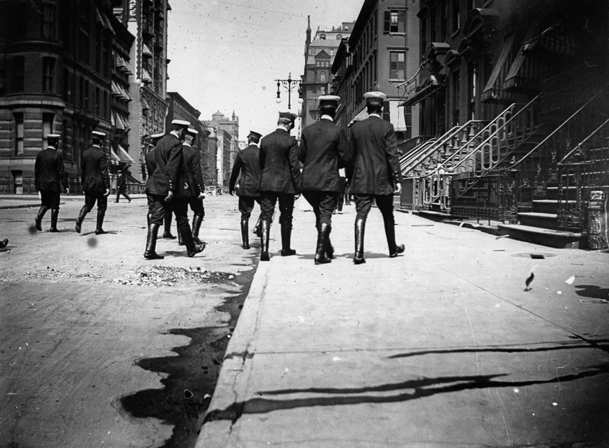 Uniformed officers in riding boots walk down a street, 1886
