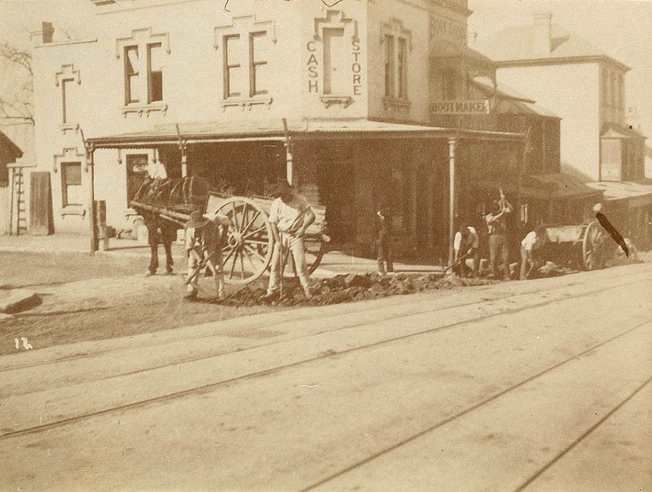 Road workers are pictured digging trenches on the side of a street in Sydney, with horses and carts parked nearby, and tramlines visible in the foreground. Photo taken circa 1885-1890