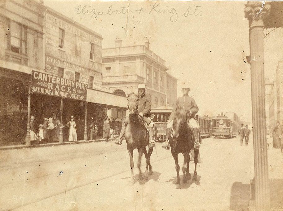 Men on horseback have been photographed at the corner of King and Elizabeth Street in Sydney in 1890, as women watch on from the side of the street and trams go past in the background